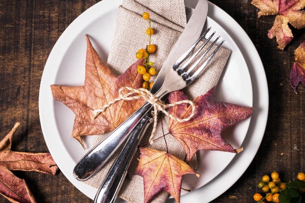 Herbst auf dem Tisch. Teller, Besteck und Serviette in herbstlichen Farben sind auf einem Holztisch arrangiert. Als Schmuck dienen Blätter und Beeren